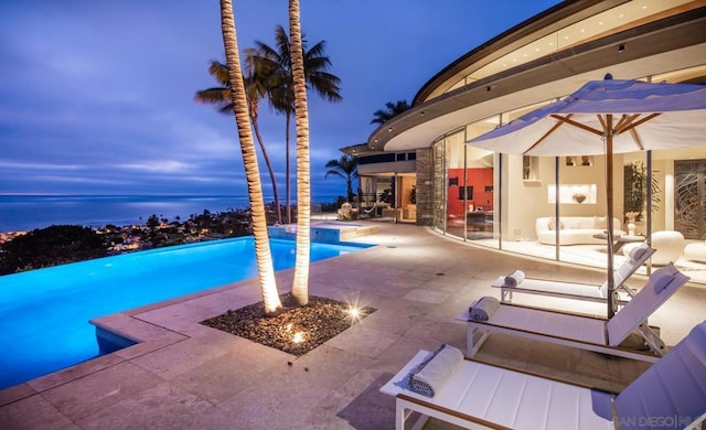 pool at dusk featuring a water view and a patio