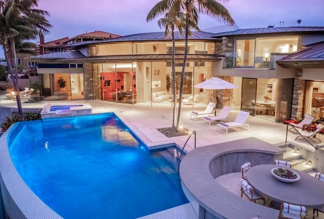 pool at dusk with an in ground hot tub, an outdoor bar, and a patio