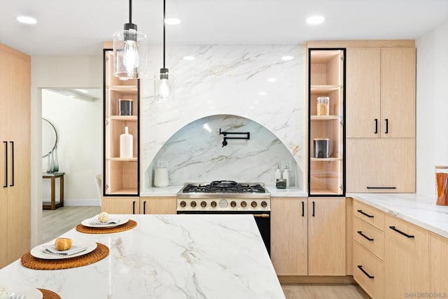 kitchen featuring pendant lighting, stainless steel range with gas stovetop, light brown cabinetry, and light stone countertops