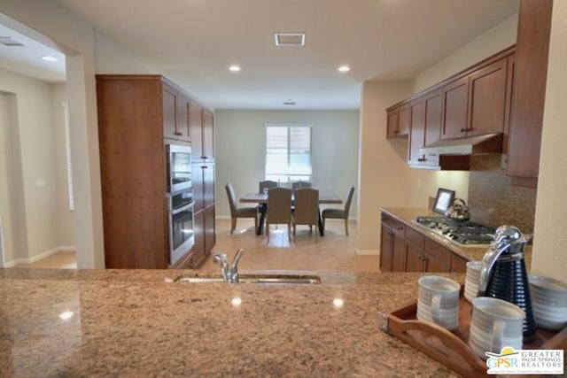 kitchen with backsplash, sink, light stone countertops, and stainless steel appliances