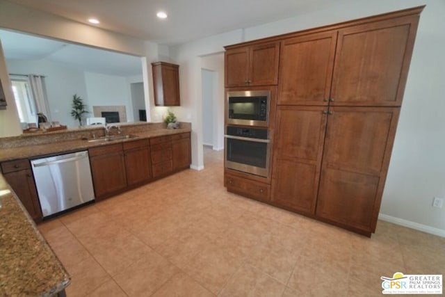 kitchen with a tile fireplace, sink, dark stone counters, lofted ceiling, and appliances with stainless steel finishes