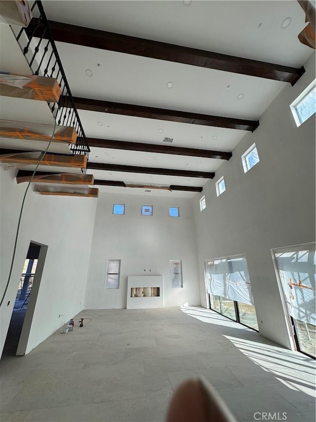 unfurnished living room with beam ceiling and a high ceiling