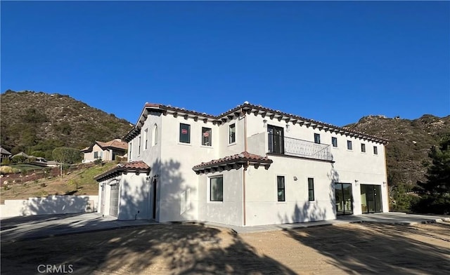 view of front facade featuring a balcony, a tiled roof, an attached garage, a mountain view, and stucco siding