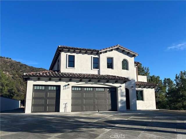 mediterranean / spanish-style home with concrete driveway, a tiled roof, and stucco siding