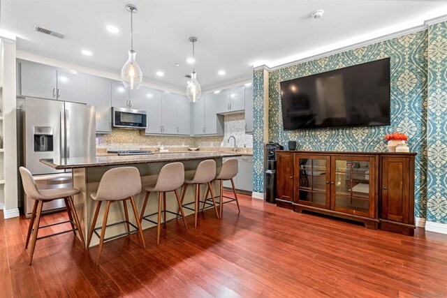 kitchen with hardwood / wood-style floors, stainless steel appliances, a kitchen breakfast bar, dark stone countertops, and hanging light fixtures