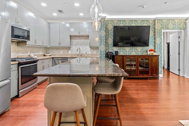 kitchen with pendant lighting, sink, light wood-type flooring, appliances with stainless steel finishes, and a breakfast bar area