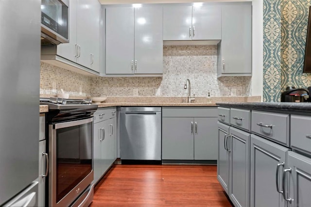 kitchen with appliances with stainless steel finishes, wood-type flooring, tasteful backsplash, sink, and gray cabinetry