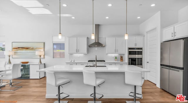 kitchen featuring wall chimney exhaust hood, appliances with stainless steel finishes, hanging light fixtures, and white cabinets