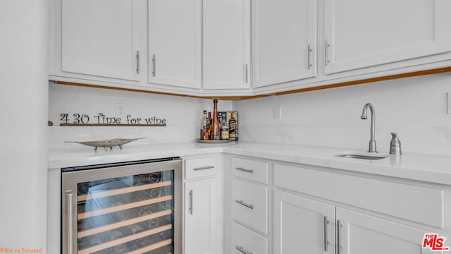 bar with wine cooler, sink, light stone counters, and white cabinets