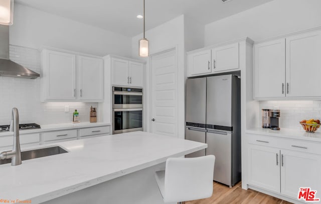 kitchen featuring appliances with stainless steel finishes, white cabinetry, sink, hanging light fixtures, and wall chimney exhaust hood