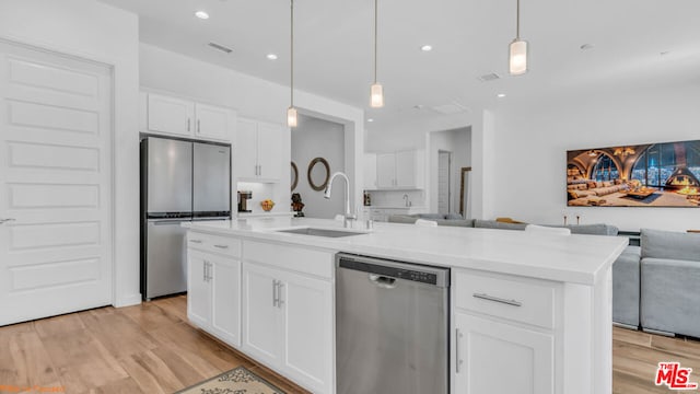 kitchen featuring appliances with stainless steel finishes, decorative light fixtures, an island with sink, sink, and white cabinets