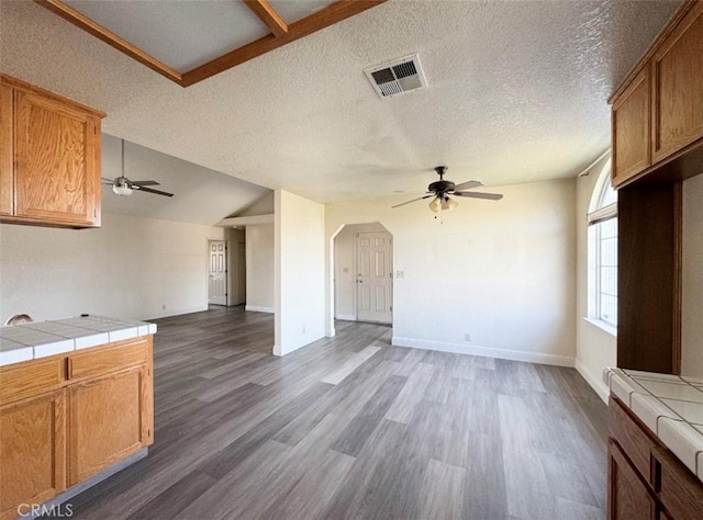 unfurnished living room with ceiling fan, dark hardwood / wood-style flooring, a textured ceiling, and vaulted ceiling