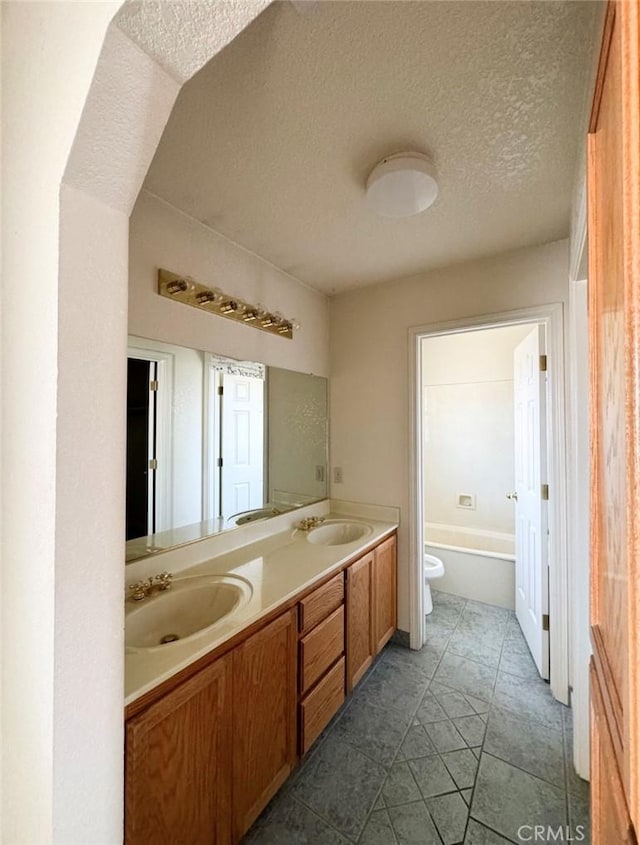 bathroom with a tub to relax in, tile patterned floors, vanity, a textured ceiling, and toilet