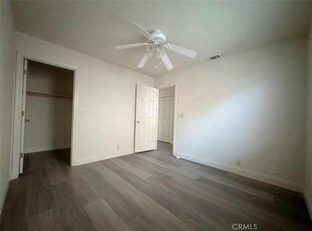 unfurnished bedroom with ceiling fan, a spacious closet, and dark hardwood / wood-style floors