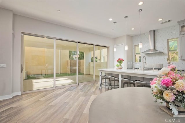 kitchen with wall chimney exhaust hood, tasteful backsplash, pendant lighting, a breakfast bar area, and light wood-type flooring