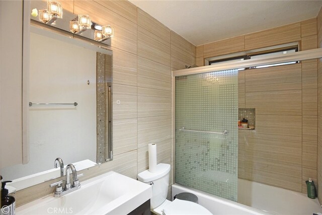 full bathroom featuring vanity, toilet, bath / shower combo with glass door, and tile walls