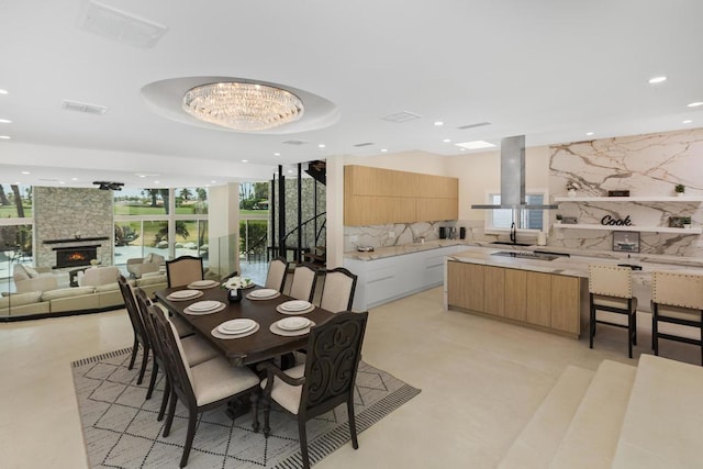 dining space with a raised ceiling, a fireplace, expansive windows, and an inviting chandelier