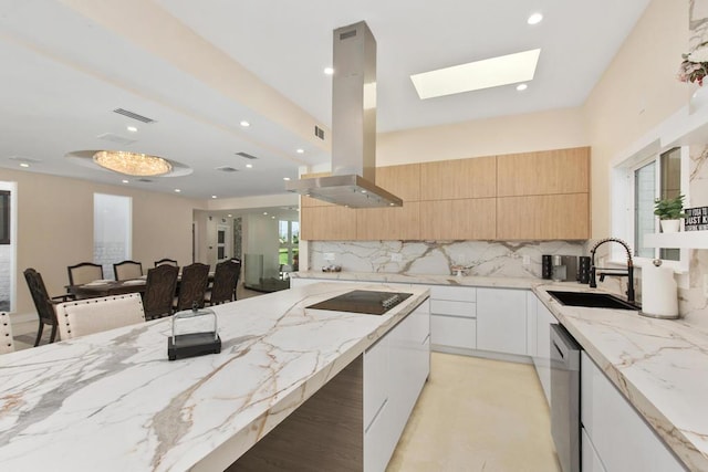 kitchen featuring a skylight, light stone countertops, tasteful backsplash, island range hood, and a breakfast bar