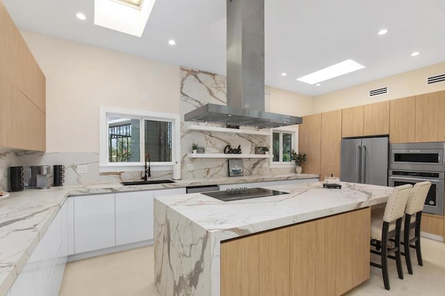 kitchen with sink, appliances with stainless steel finishes, island range hood, light stone counters, and white cabinetry