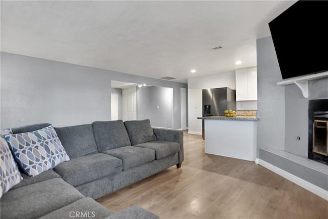 living room featuring light wood finished floors, recessed lighting, a fireplace with raised hearth, visible vents, and baseboards