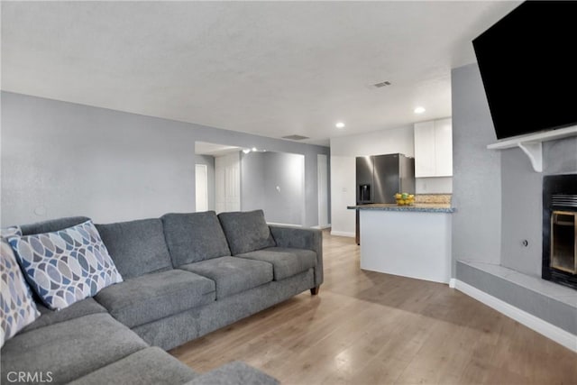 living room featuring recessed lighting, baseboards, a fireplace with raised hearth, and light wood-style flooring