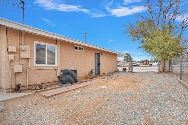 back of property with driveway, fence, cooling unit, and stucco siding