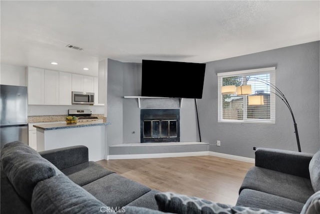 living area featuring visible vents, baseboards, a glass covered fireplace, light wood-style flooring, and recessed lighting