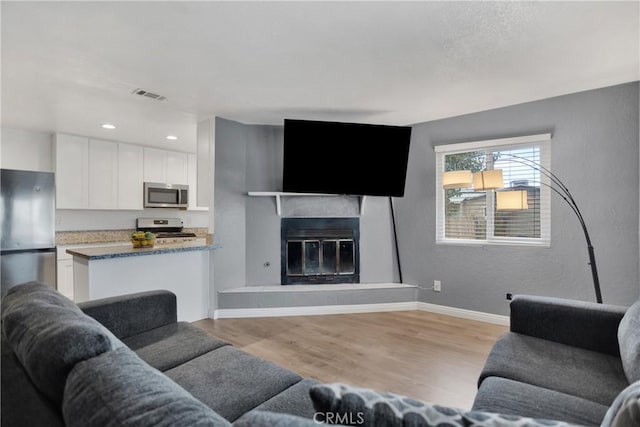 10590 Navajo Rd, Apple Valley, CA 92308 - living area featuring light wood-style flooring, baseboards, a glass covered fireplace, a textured wall, and recessed lighting