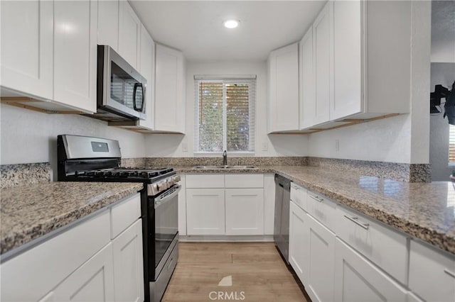 kitchen with light wood-type flooring, light stone countertops, appliances with stainless steel finishes, and white cabinets