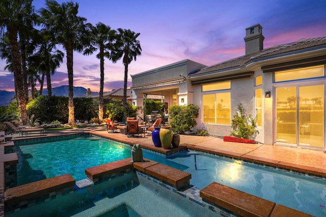 pool at dusk featuring an in ground hot tub and a patio