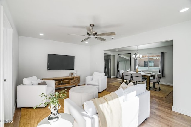 living room with ceiling fan with notable chandelier and light hardwood / wood-style floors