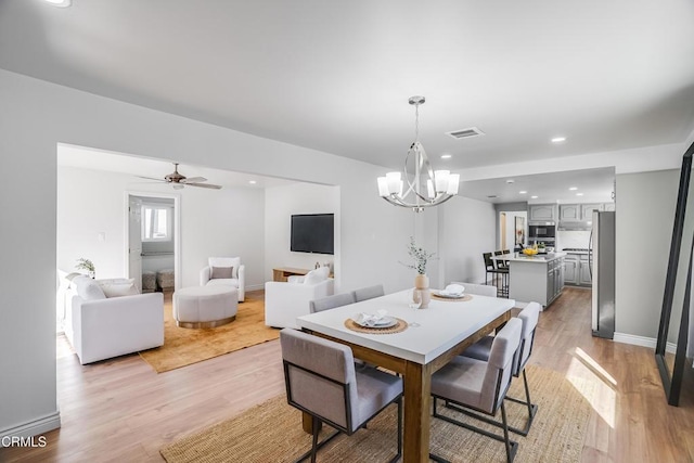 dining room featuring ceiling fan with notable chandelier and light hardwood / wood-style floors