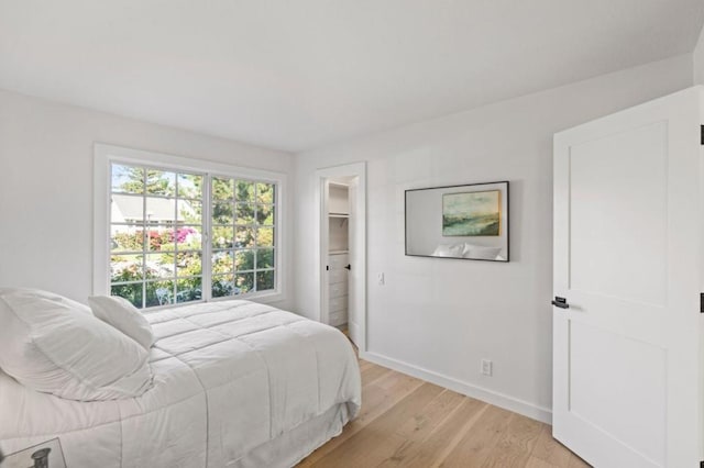 bedroom with a walk in closet, light wood-type flooring, and a closet