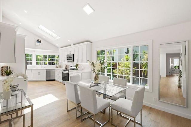 dining room featuring light wood-type flooring, a skylight, high vaulted ceiling, and sink