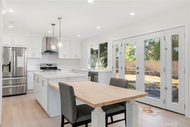 kitchen featuring a kitchen island, white cabinetry, hanging light fixtures, appliances with stainless steel finishes, and wall chimney exhaust hood