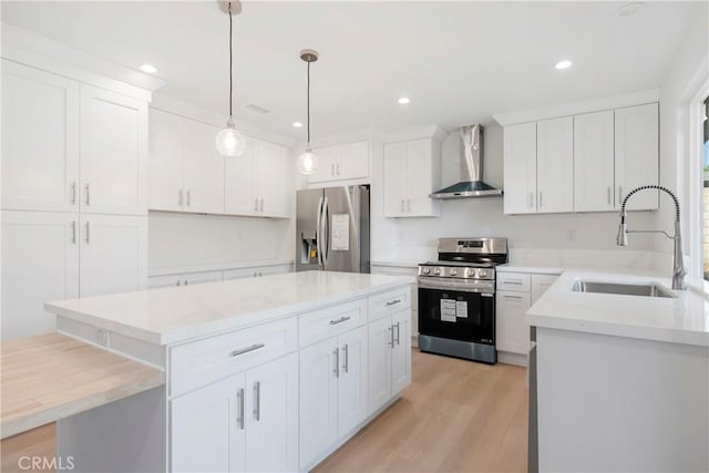 kitchen featuring wall chimney range hood, a center island, sink, appliances with stainless steel finishes, and white cabinets