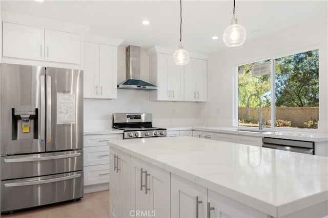 kitchen featuring stainless steel appliances, decorative light fixtures, wall chimney exhaust hood, white cabinets, and sink