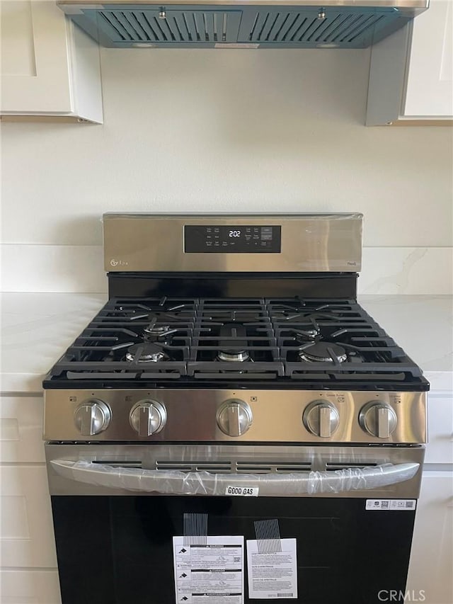 interior details with stainless steel gas stove, white cabinets, and exhaust hood