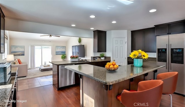 kitchen with sink, a center island, a kitchen breakfast bar, dark hardwood / wood-style floors, and appliances with stainless steel finishes