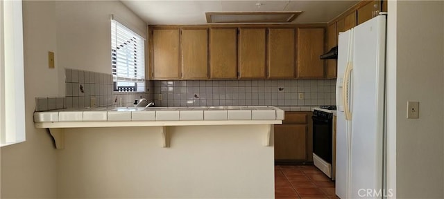 kitchen with white appliances, a kitchen breakfast bar, decorative backsplash, dark tile patterned floors, and tile counters