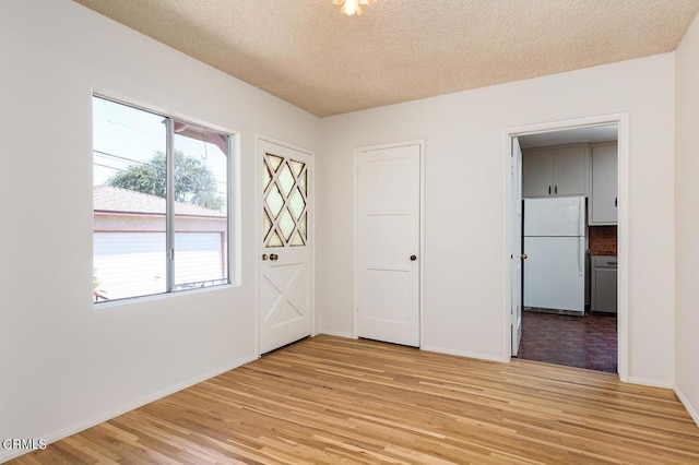 unfurnished bedroom featuring light hardwood / wood-style flooring, white fridge, and a textured ceiling