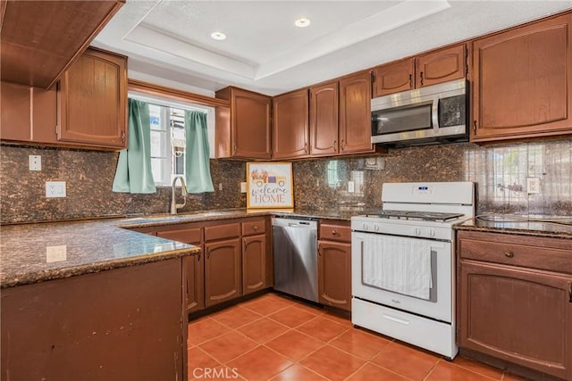 kitchen featuring sink, light tile patterned floors, stainless steel appliances, decorative backsplash, and a raised ceiling