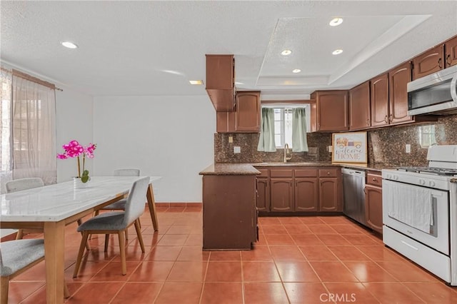 kitchen with stainless steel appliances, a tray ceiling, tile patterned flooring, and backsplash