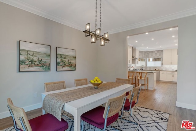 dining area with crown molding, sink, light hardwood / wood-style floors, and a notable chandelier