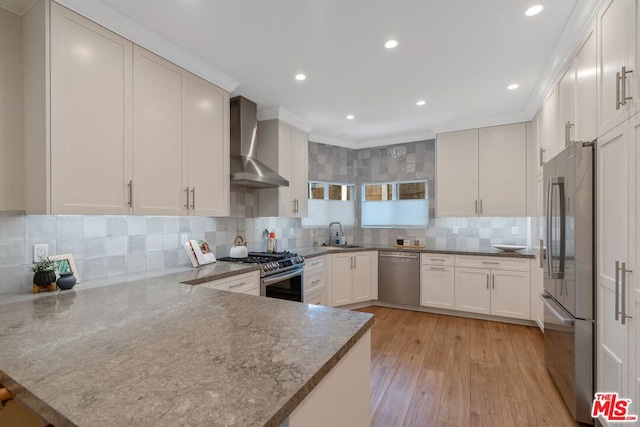 kitchen featuring kitchen peninsula, wall chimney exhaust hood, stainless steel appliances, light hardwood / wood-style floors, and white cabinetry