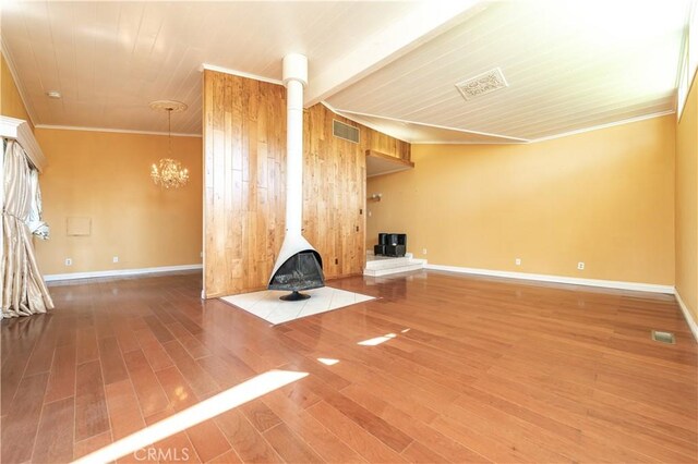 unfurnished living room with hardwood / wood-style flooring, a notable chandelier, a wood stove, and crown molding