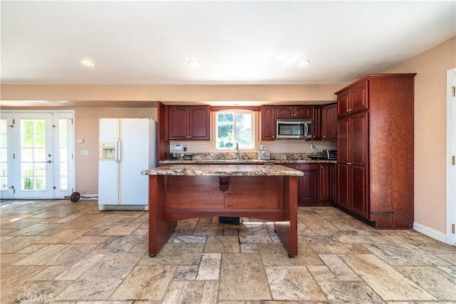 kitchen featuring white fridge with ice dispenser, sink, light stone counters, a breakfast bar, and a kitchen island