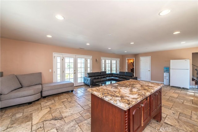 kitchen featuring french doors, white fridge, light stone counters, and a kitchen island