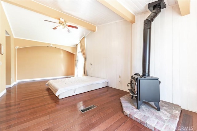 bedroom featuring a wood stove, ceiling fan, and dark wood-type flooring