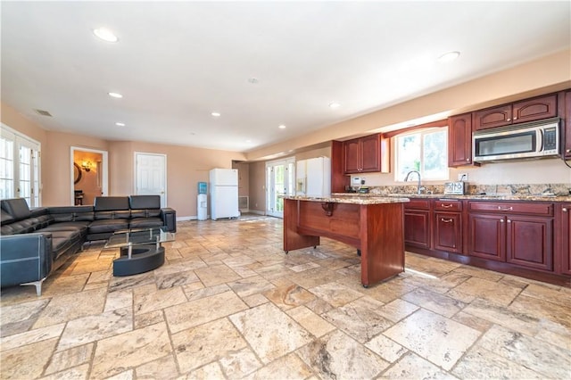 kitchen with a center island, sink, white fridge, light stone counters, and a breakfast bar area